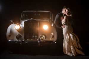 A bride and groom share a romantic kiss in front of a vintage car at their beautiful New York wedding.