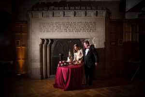 A wedding couple standing in front of a fireplace.