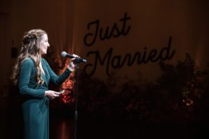 A woman in a green dress singing into a microphone at a wedding in New York.