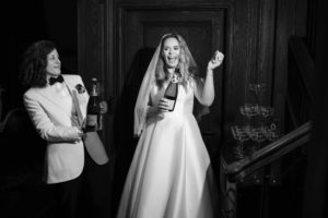 A bride and groom in New York are holding champagne bottles in front of a staircase.