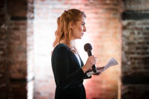 A woman is holding a microphone in front of a brick wall in New York.