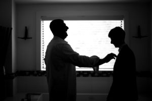 A silhouette of a man putting on a tie in a bathroom for his wedding in New York.