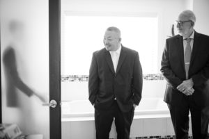 Two men in suits standing next to each other in a bathroom at a wedding in New York.