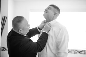 In a wedding venue in New York City, one man carefully adjusts another man's tie in the bathroom before the ceremony.