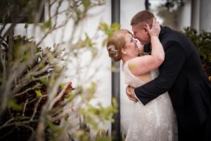 A newlywed couple sharing a passionate kiss amidst lush greenery at their wedding in New York.