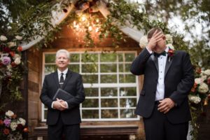 The groom in a tuxedo is wiping his eyes during the emotional wedding ceremony.