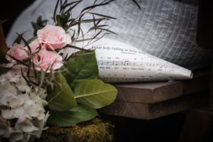 A wedding bouquet of flowers and a sheet of music sits on a wooden bench in New York.