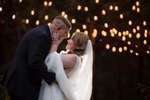 A bride and groom embrace in front of string lights at their New York wedding celebration.