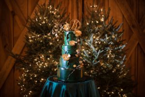 A green wedding cake sits on top of a table in front of Christmas trees in New York.