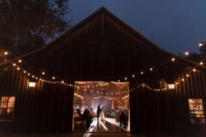 A bride and groom standing in front of a barn at their wedding in New York.