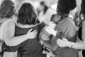 A black and white photo of a group of women hugging a baby in New York.