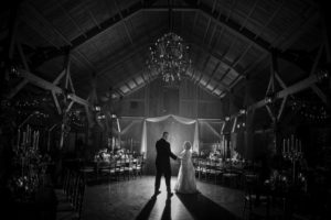 A bride and groom standing in front of a large barn at their New York wedding.
