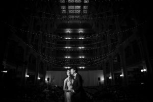 A bride and groom share a romantic kiss during their enchanting wedding ceremony in a dimly lit room.