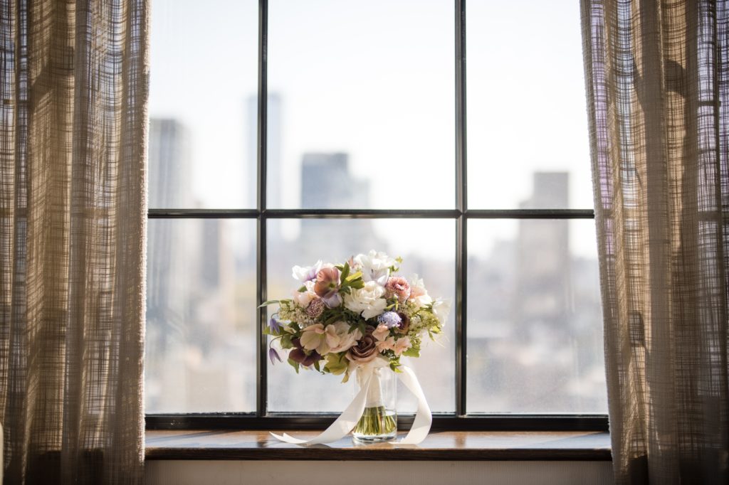 A wedding bouquet sits on a window sill with a view of the city of New York.