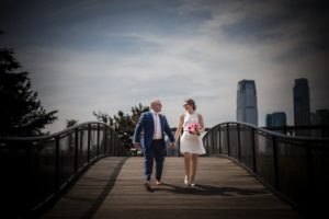 A newlywed couple walking on a bridge in front of the iconic New York City skyline on their wedding day.
