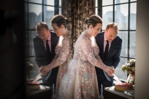 A newlywed couple joyfully cutting a wedding cake in front of a mirror.
