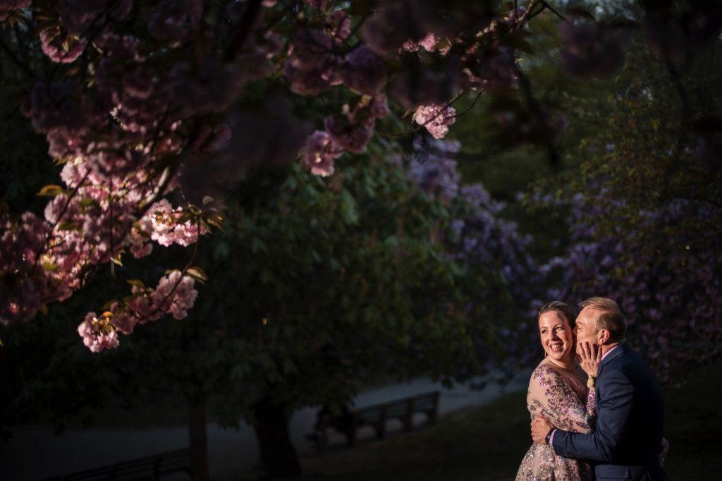 A bride and groom embrace under a cherry blossom tree in New York City, celebrating their wedding day.