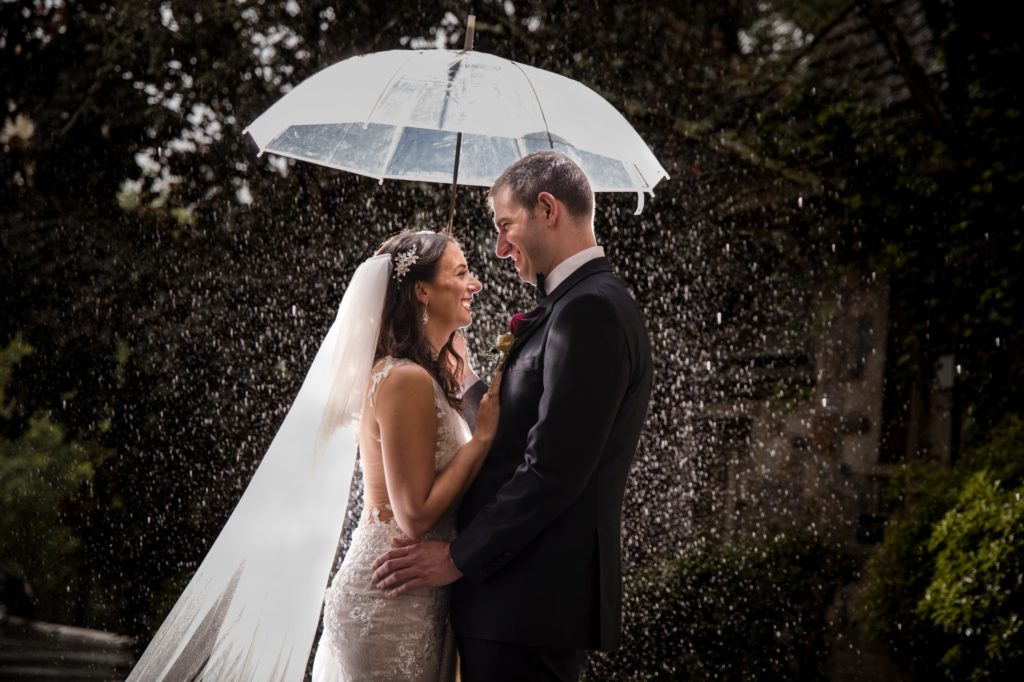 A bride and groom standing under an umbrella in the rain on their wedding day in New York.