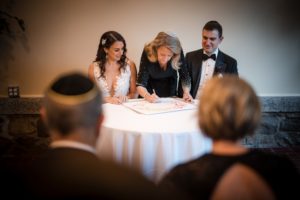 A bride and groom, in New York, signing a wedding certificate at a table.