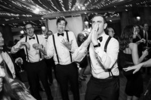 A black and white photo of a group of men dancing at a wedding in New York.