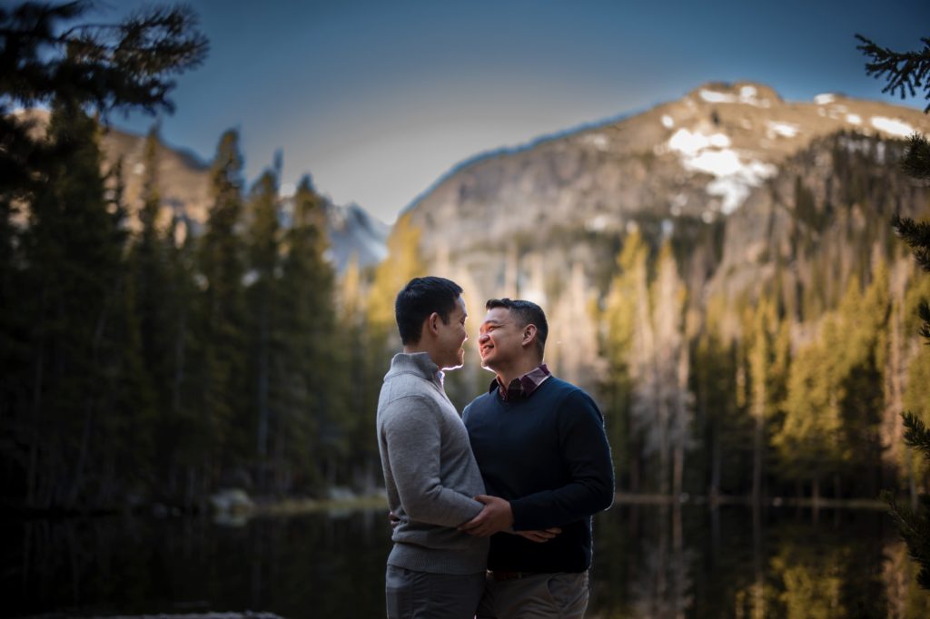 Two men hugging in front of a lake at their wedding in the mountains of New York.