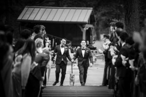 A black and white photo of two men walking down the aisle with a dog in New York City.