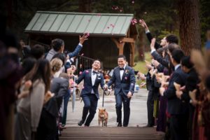 Two grooms walking down a path in New York with confetti thrown at them during their wedding.