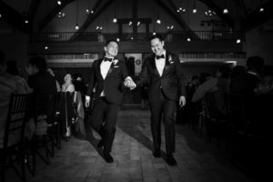 Two men in tuxedos walking down the wedding aisle in New York.