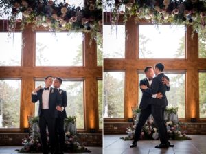 Two grooms hugging in front of a large window at their New York wedding.