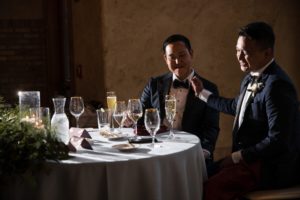 Two men in tuxedos sitting at a wedding table.