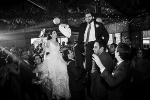 A bride and groom are being carried by a man in a black and white wedding photo.