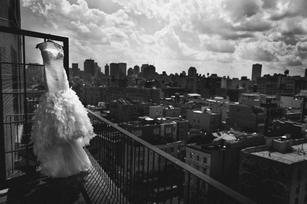 A black and white photo of a wedding dress hanging on a balcony at the Bowery Hotel.