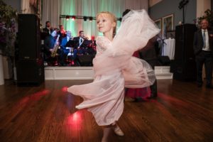 A little girl in a pink dress joyfully dancing on the dance floor at a wedding in New York.