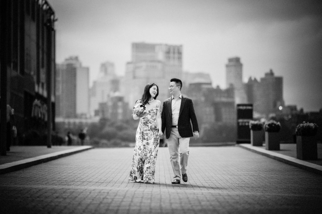 A black and white photo of a couple walking in front of a city skyline, capturing the romance of their wedding day in New York.