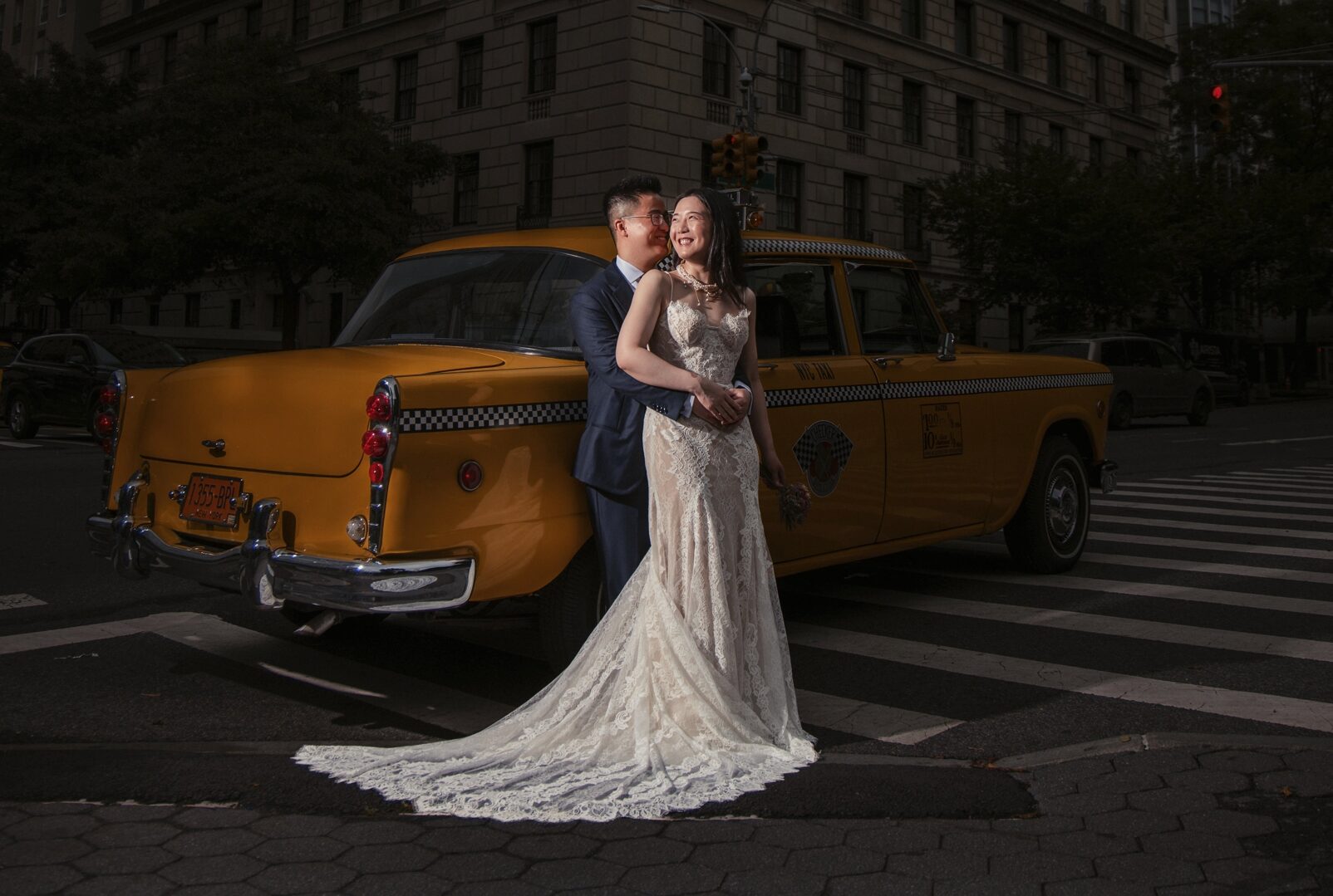 A newlywed couple poses in front of a yellow taxi in New York City on their wedding day.