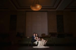 A new york bride and groom sitting on a couch in a dark room during their wedding.