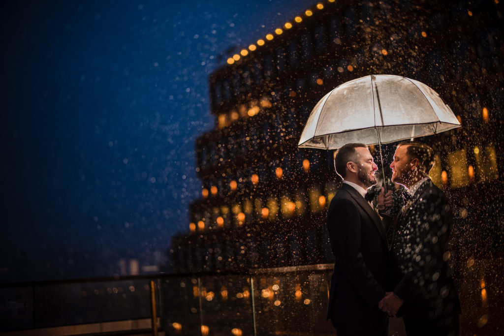 A wedding couple kissing under an umbrella in the rain in New York City.