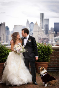 A couple and their pet dog share a special moment during their first look before their wedding, against the backdrop of a city skyline.