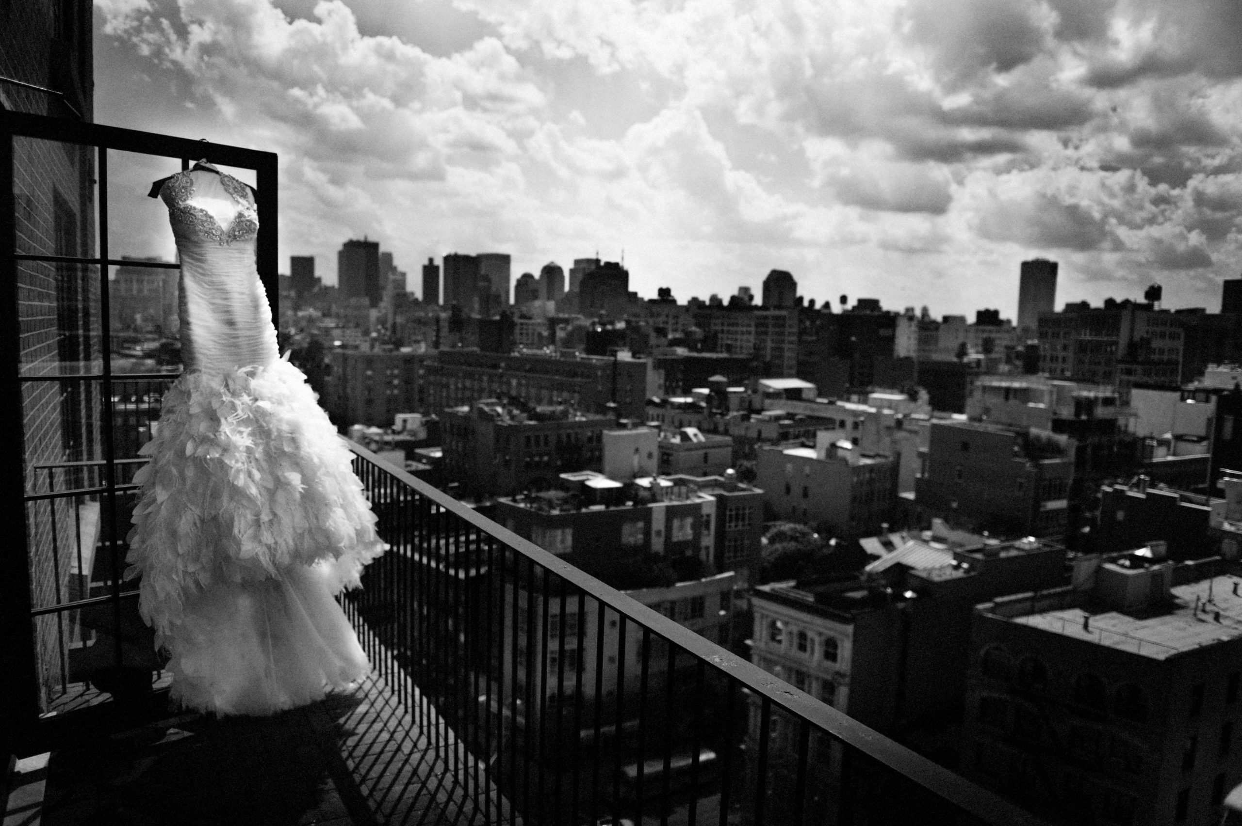 A wedding dress hangs on a balcony railing overlooking a cityscape under a cloudy sky. A wedding dress hangs on a balcony railing overlooking a cityscape under a cloudy sky.