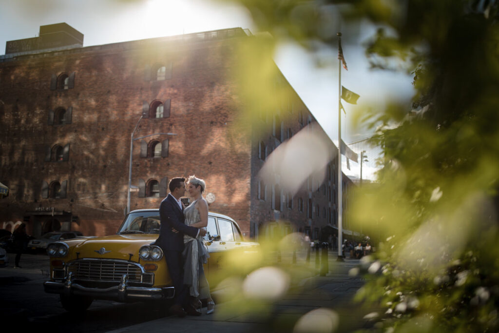 A couple standing close together leaning on an old school taxi.