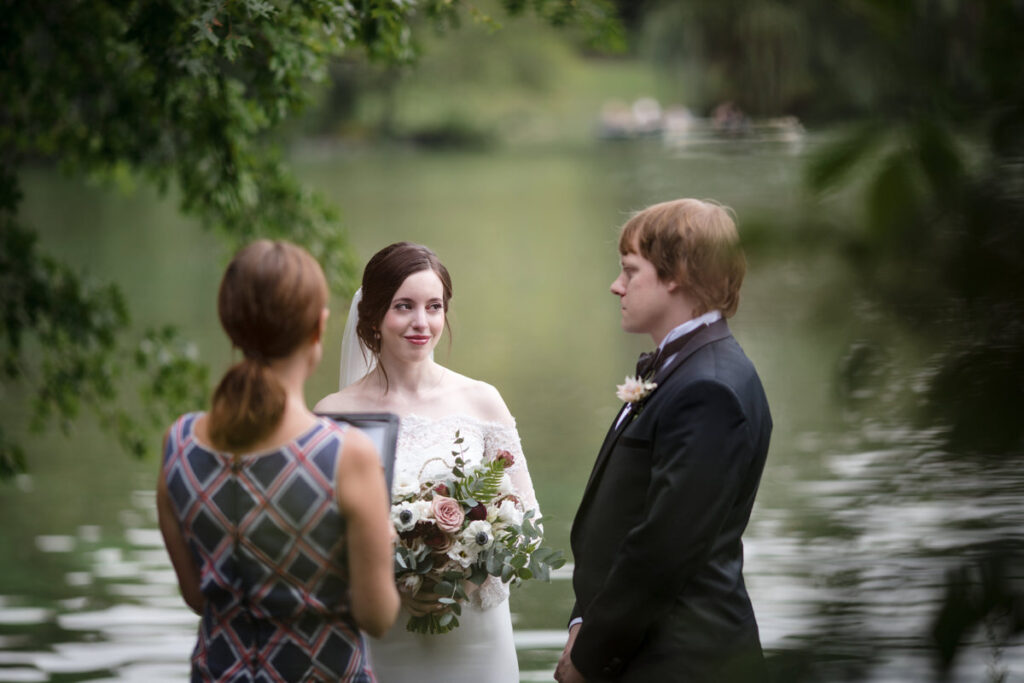 A couple standing with an officiant at a small elopement ceremony next to a lake.