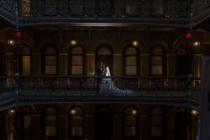 A bride and groom standing on an indoor balcony of a luxury hotel.