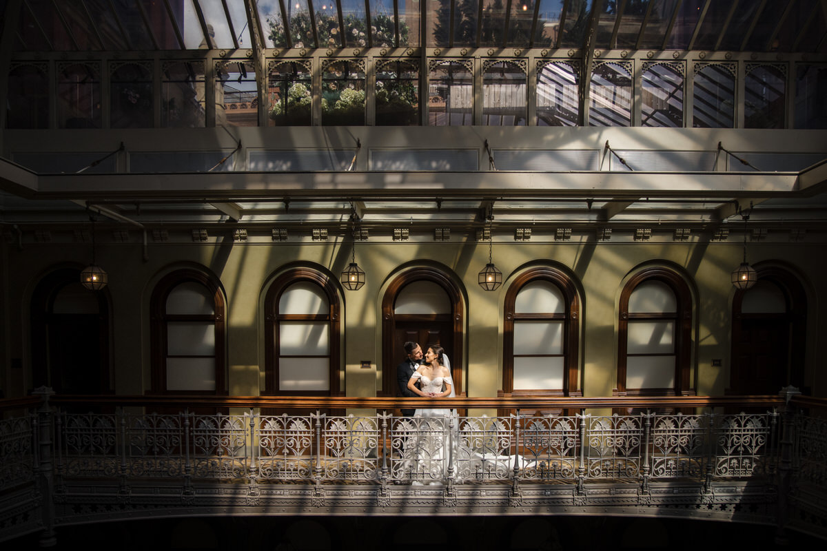 A wedding couple standing at the railing of an indoor balcony in one of the secret places to take pictures in NYC.