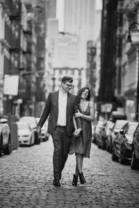 A couple holding hands and walking down a cobblestone city street.