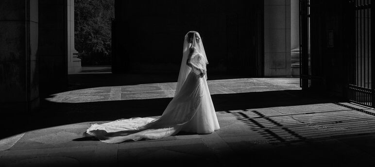 A bride in a wedding dress standing in the outdoor foyer of a large building.