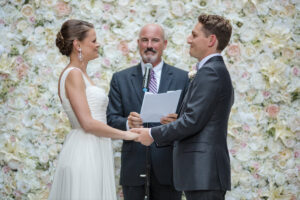 A bride and groom holding hands as their officiant stands behind them.