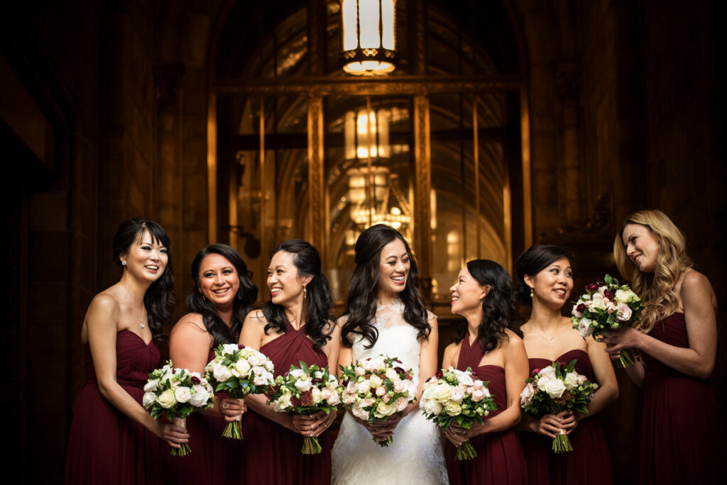 A bride and her bridesmaids standing in a line as they all hold bouquets of flowers.