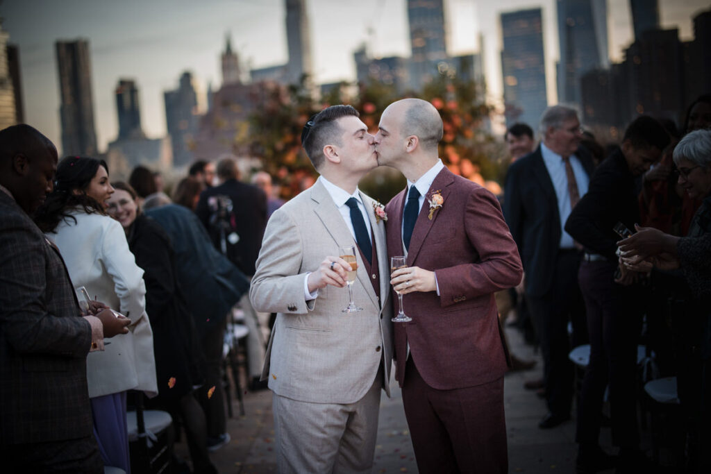 Two grooms kissing while holding champagne glasses.