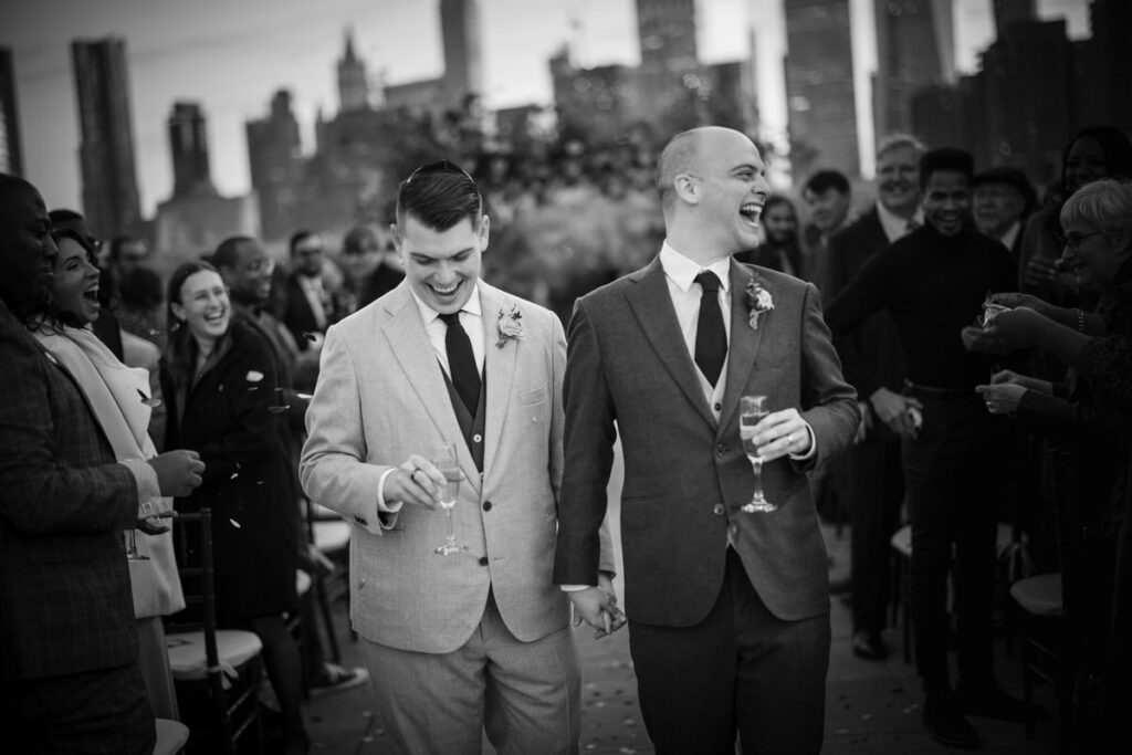 Two grooms holding champagne glasses walking back up the aisle.