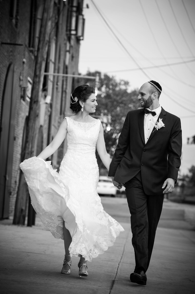 A bride and groom holding hands and walking along a sidewalk. 